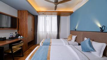 Een hotelkamer met twee bedden, een bureau met stoel, een televisie en een plafondventilator.
