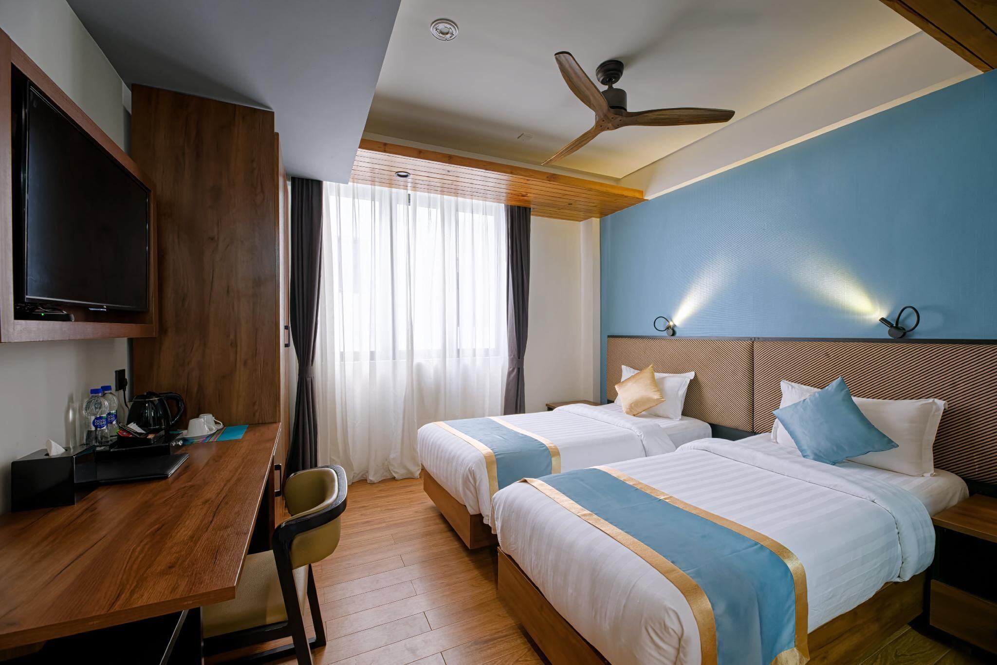 Een hotelkamer met twee bedden, een bureau, een televisie en een plafondventilator.