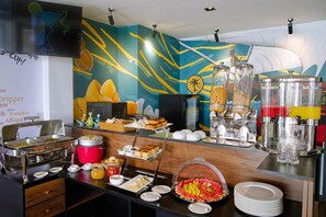 A buffet setup with various food items and beverages, including a red hot pot, a glass jar of pickles, and a fruit bowl. - H78 Veli (Hulhumale)