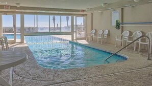 An indoor swimming pool with clear views of the ocean, a poolside seating area, and an exit sign. - Tradewinds 603 (Orange Beach)