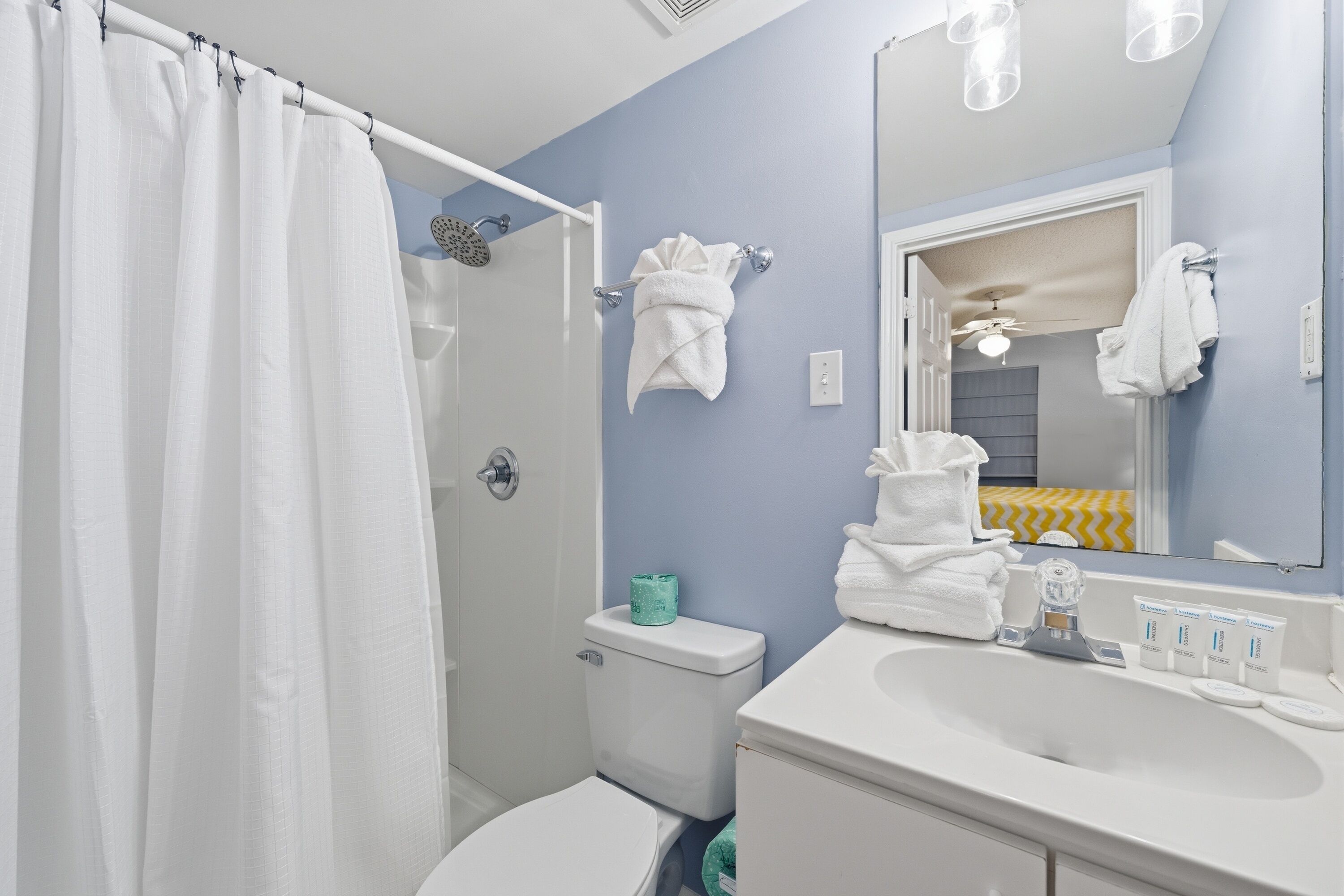 Un baño con cortina de ducha, inodoro, lavabo con artículos de aseo y espejo.