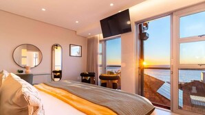 Une chambre avec un lit, une télévision, une grande fenêtre donnant sur la mer et un balcon.