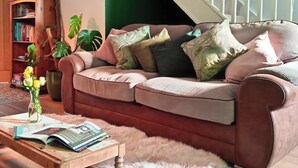 A living room with a brown leather sofa, a wooden coffee table, a green wall, a staircase with white railings, and a clock on the wall. - Soak in amazing views @ EbbandFlow (Newquay)