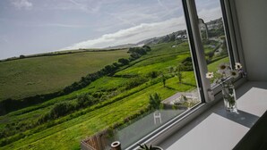 A view from a window overlooking a green landscape with a clear sky. - Soak in amazing views @ EbbandFlow (Newquay)