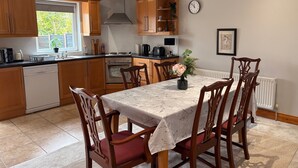 Une cuisine avec des meubles de rangement en bois, une table à manger avec des chaises, une horloge au mur et un radiateur.