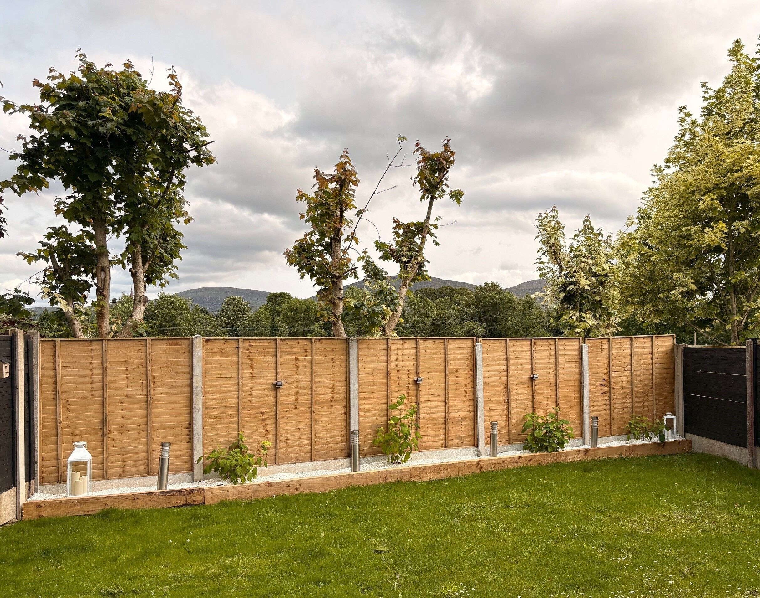 A wooden fence with a metal gate, a grassy lawn, and trees in the background.