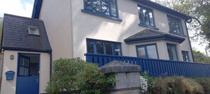 A two-story house with a blue door and windows, a stone wall, and a blue fence.