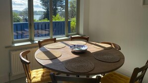 A dining area with a round table, six chairs, and a view of a lake through large windows.