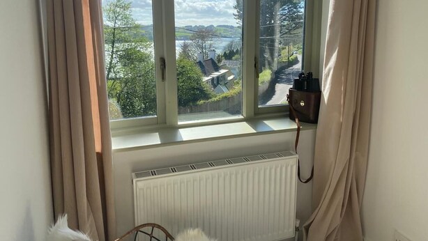 A room with a large window overlooking a scenic landscape, a radiator below the window, and a chair in the foreground.
