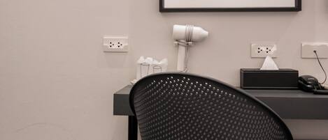 Una silla de oficina moderna con respaldo perforado, un escritorio con una computadora y una lámpara, un cesto de basura y un cuadro en la pared.
