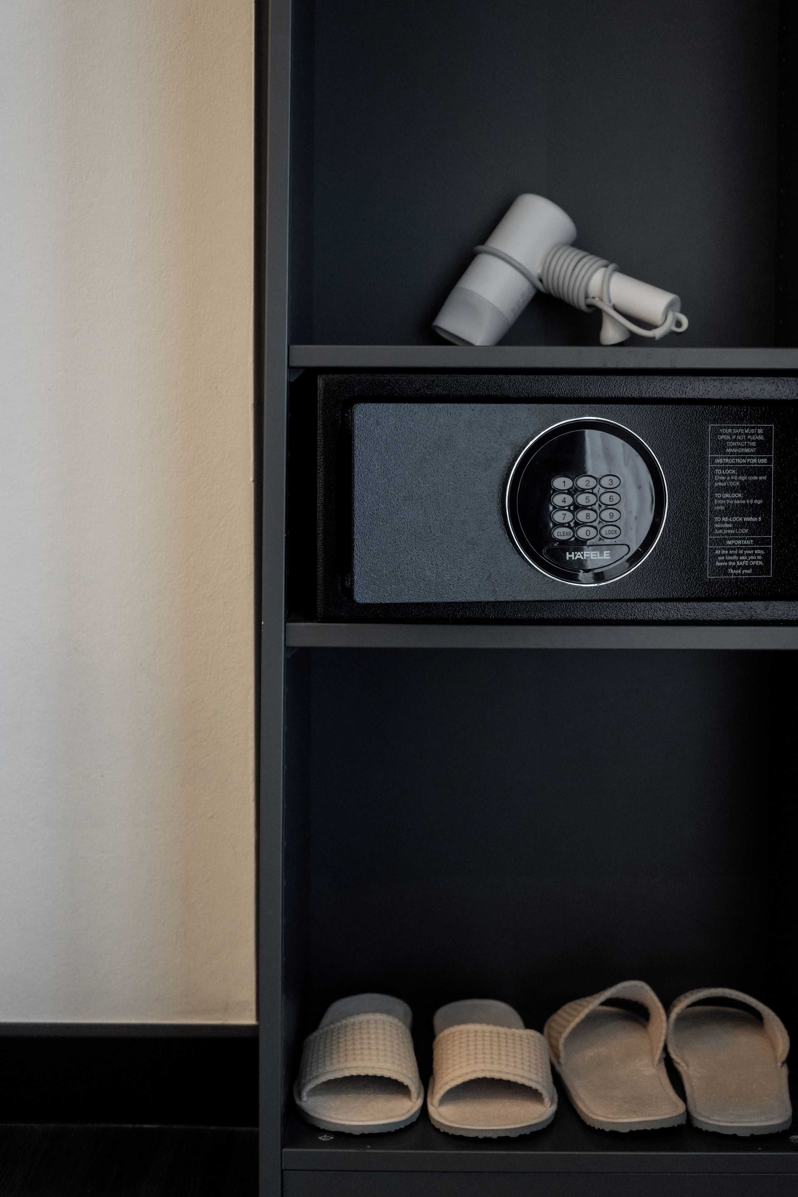 A black shelf with a hairdryer, a safe, and a pair of slippers.