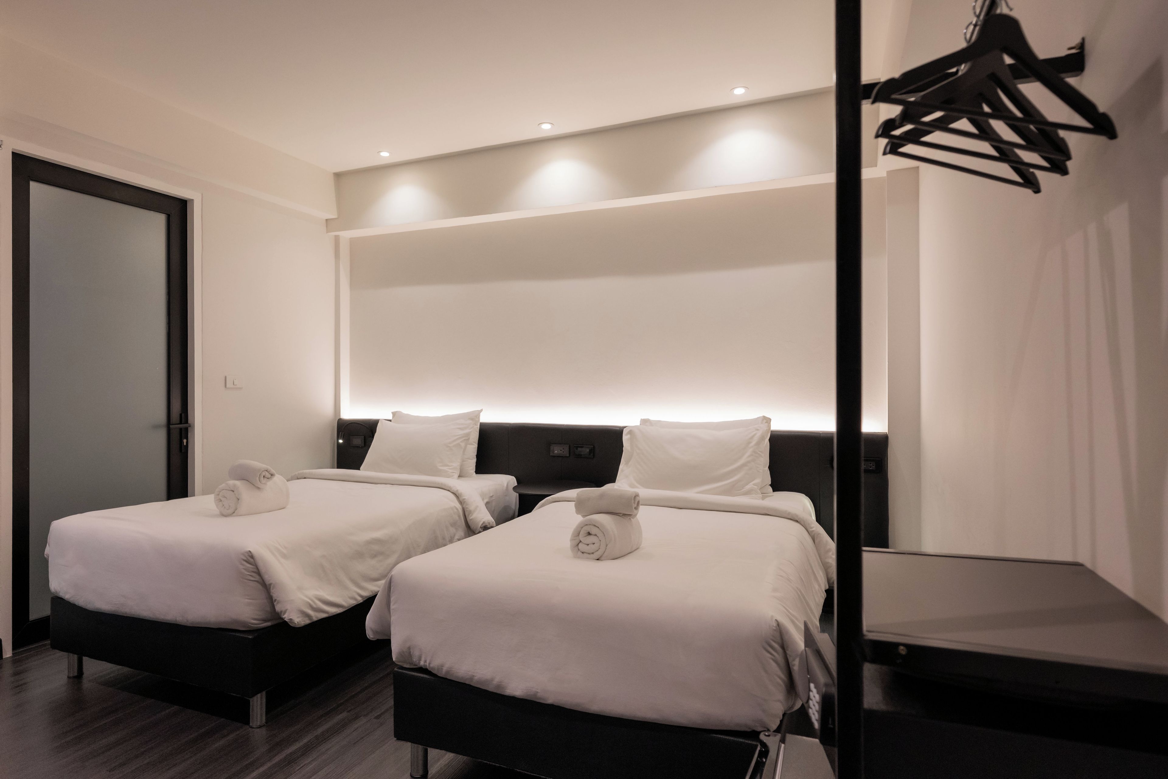 A hotel room with two beds, a dark headboard, and a wall-mounted light fixture.