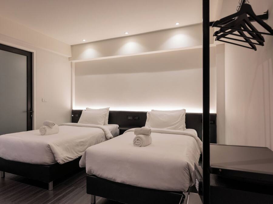 A hotel room with two beds, a dark headboard, and a wall-mounted light fixture.