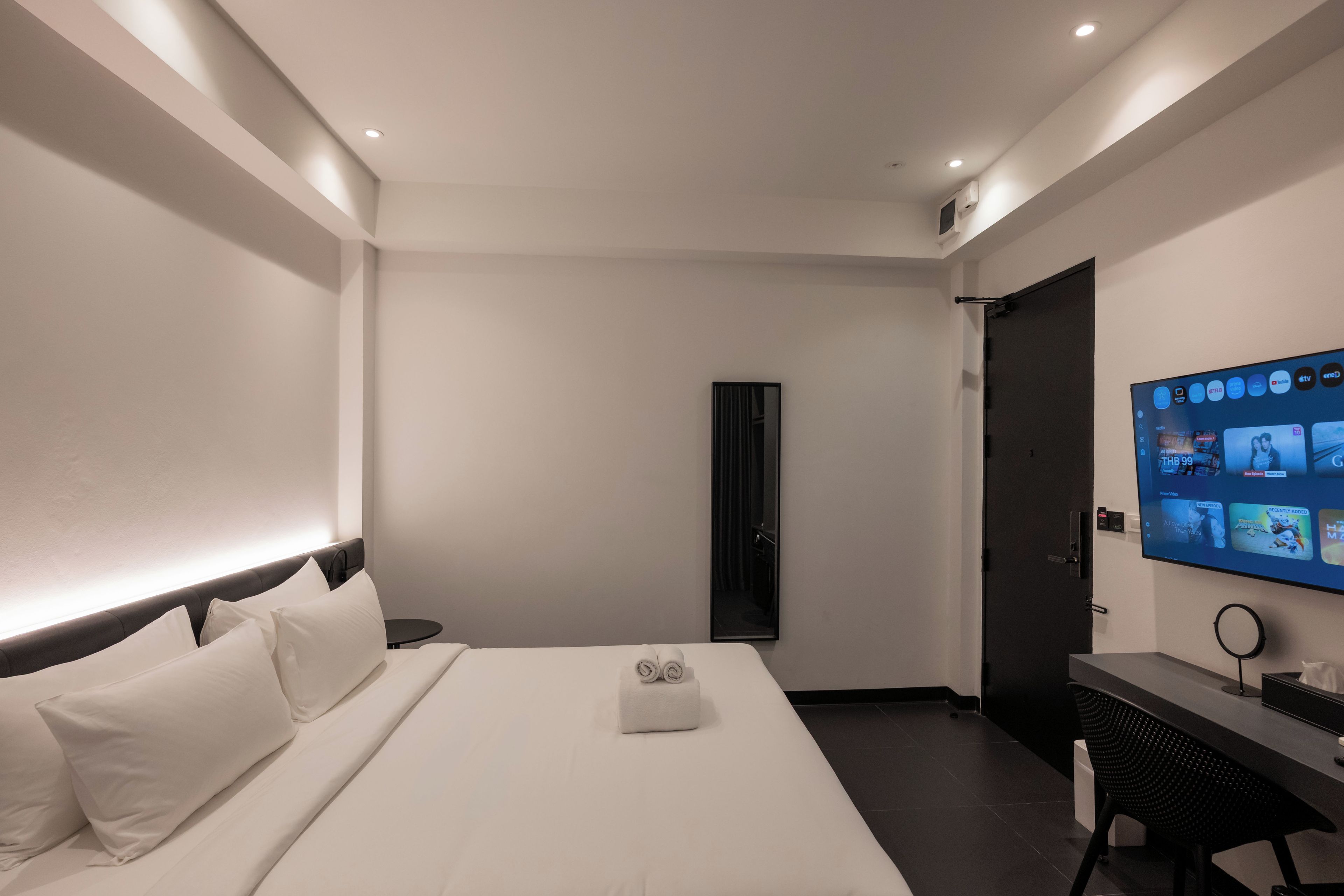A hotel room with a bed, a desk, a TV, and a door.