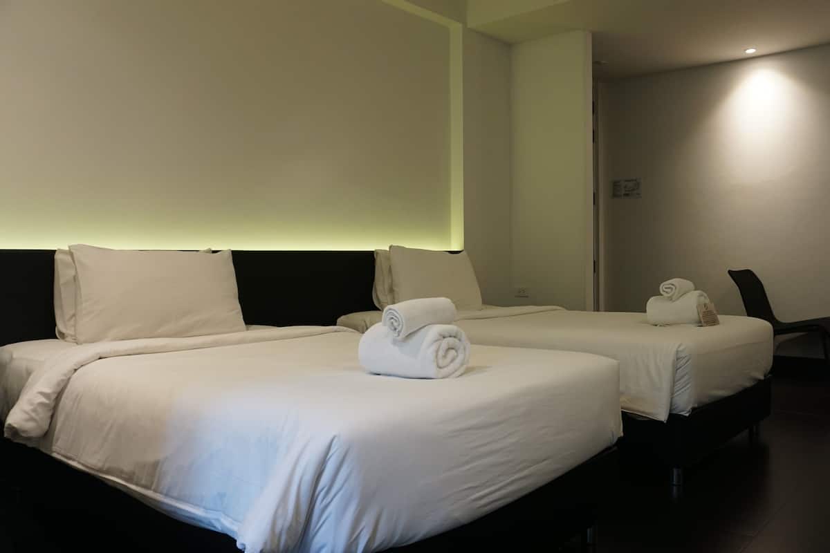 A hotel room with two beds, each with white linens and rolled towels.