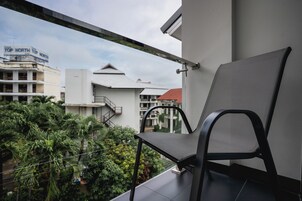 A balcony with a chair, overlooking a residential area with buildings and greenery.