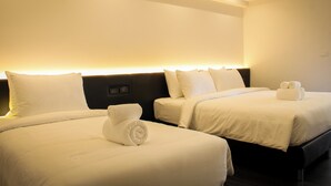Habitación de hotel con dos camas, cada una con sábanas y almohadas blancas, y una cama bien hecha con una toalla enrollada.