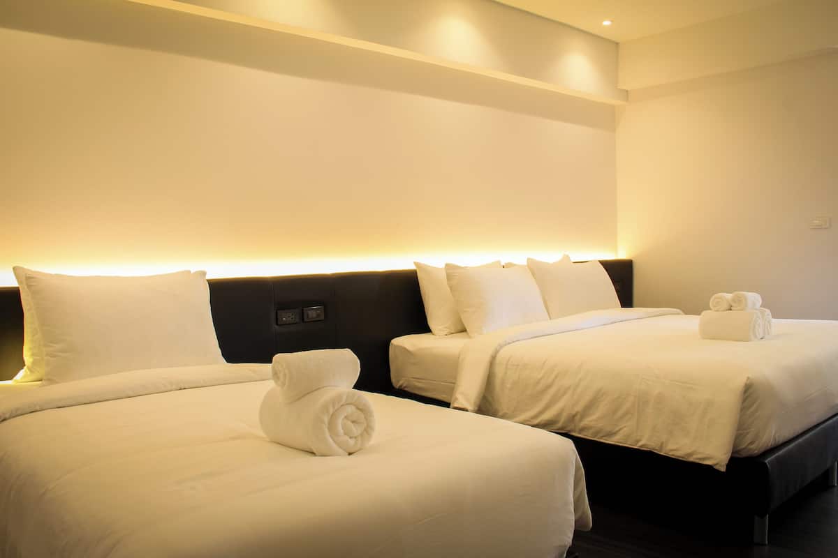 A hotel room with two beds, each with white linens and pillows, and a neatly made bed with a rolled towel.