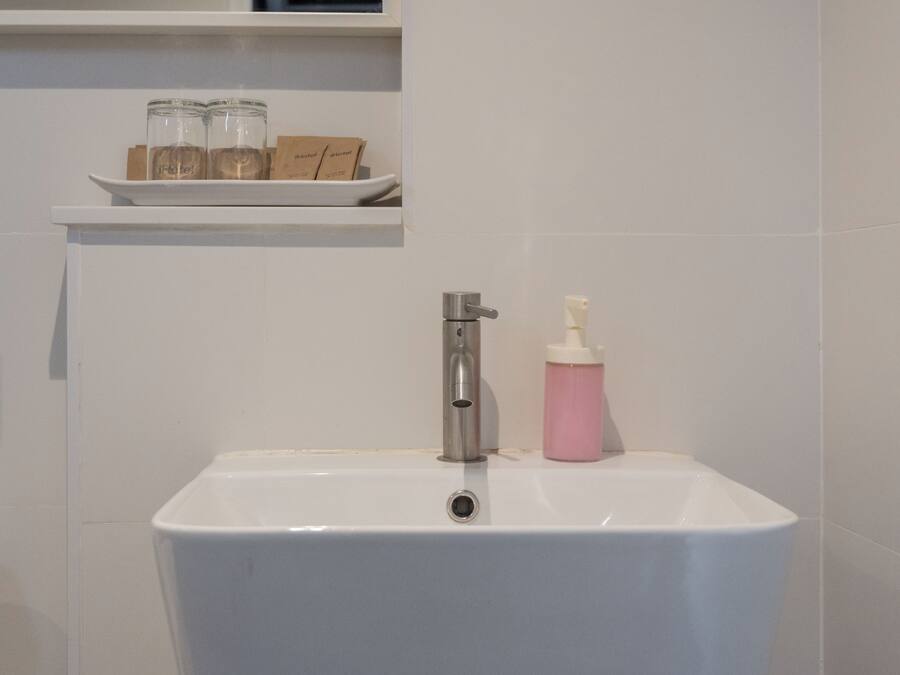 A bathroom with a white sink, a mirror above it, and a shelf with a glass and a tissue box.