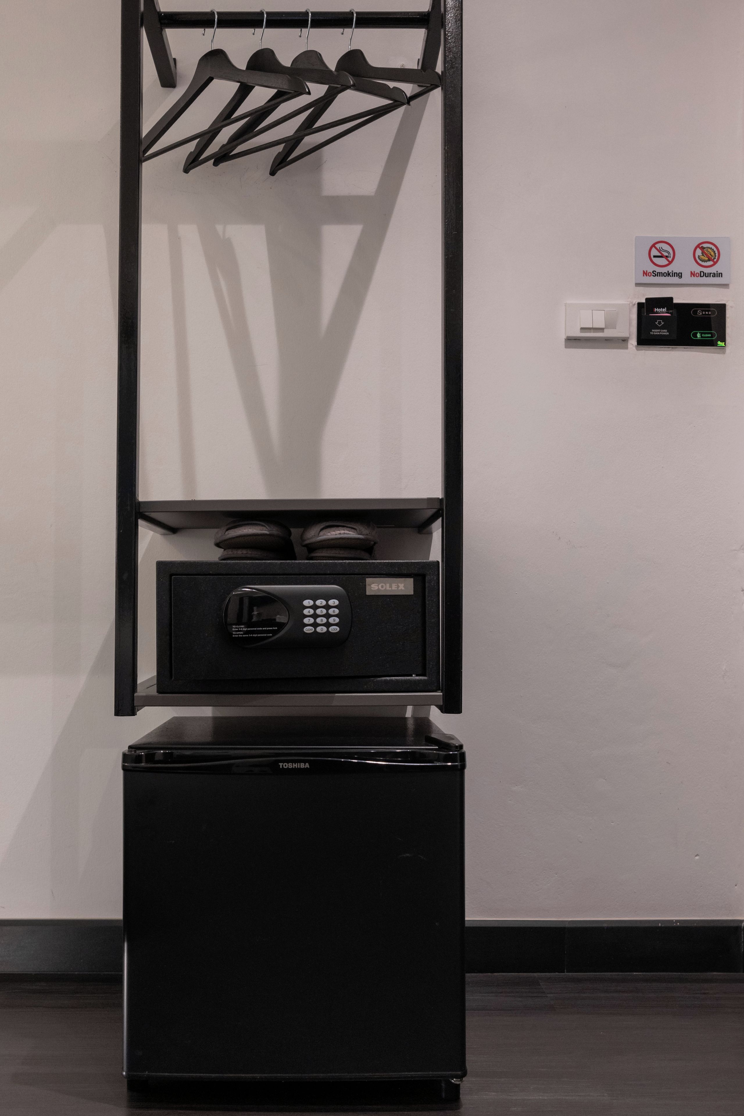 Habitación de hotel con minibar, refrigerador de minibar, zapatero y letrero de prohibición de fumar y durián.