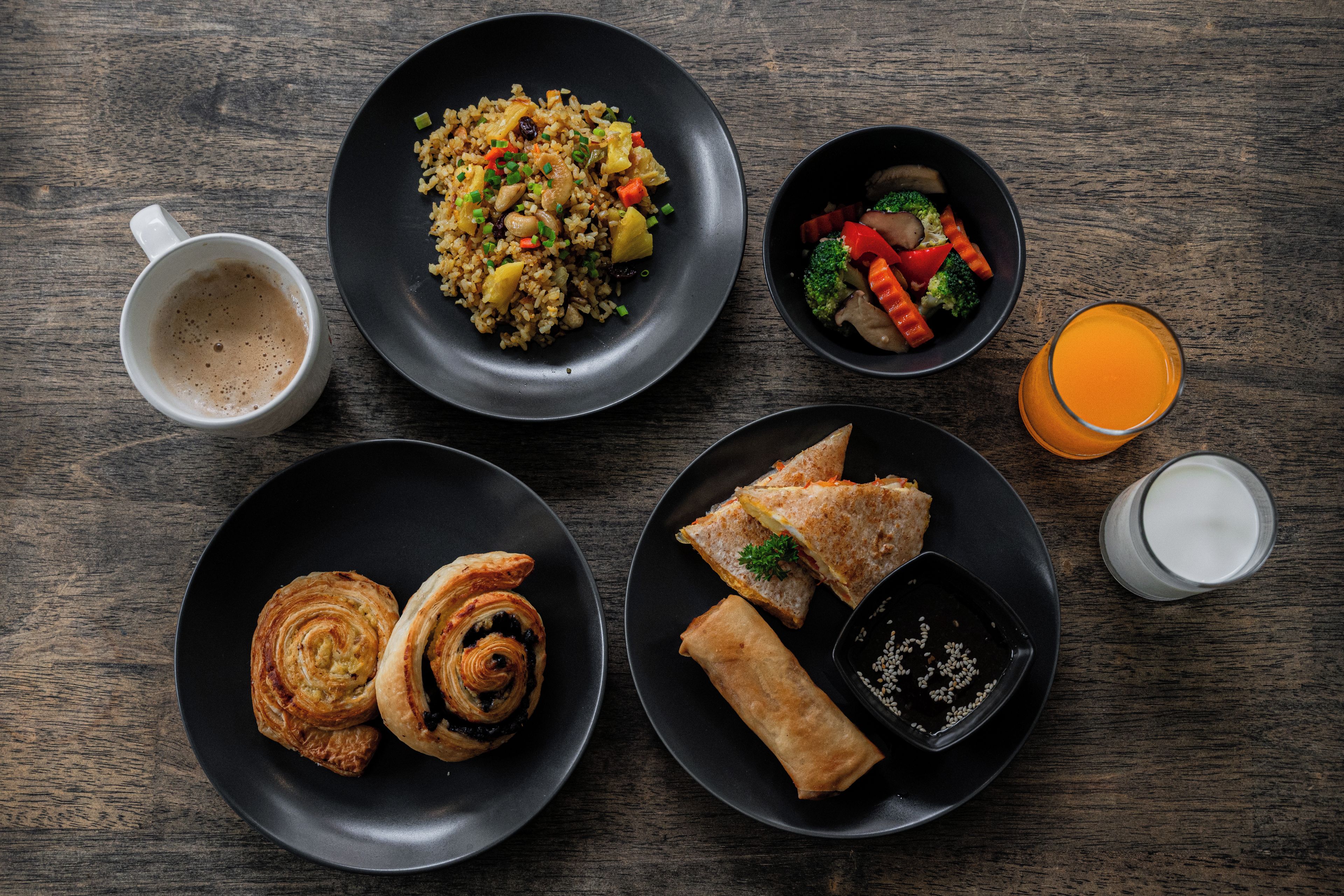 A table with various dishes including fried rice, vegetables, pastries, and a glass of orange juice.
