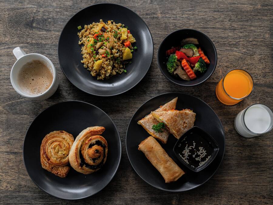A table with various dishes including fried rice, vegetables, pastries, and a glass of orange juice.