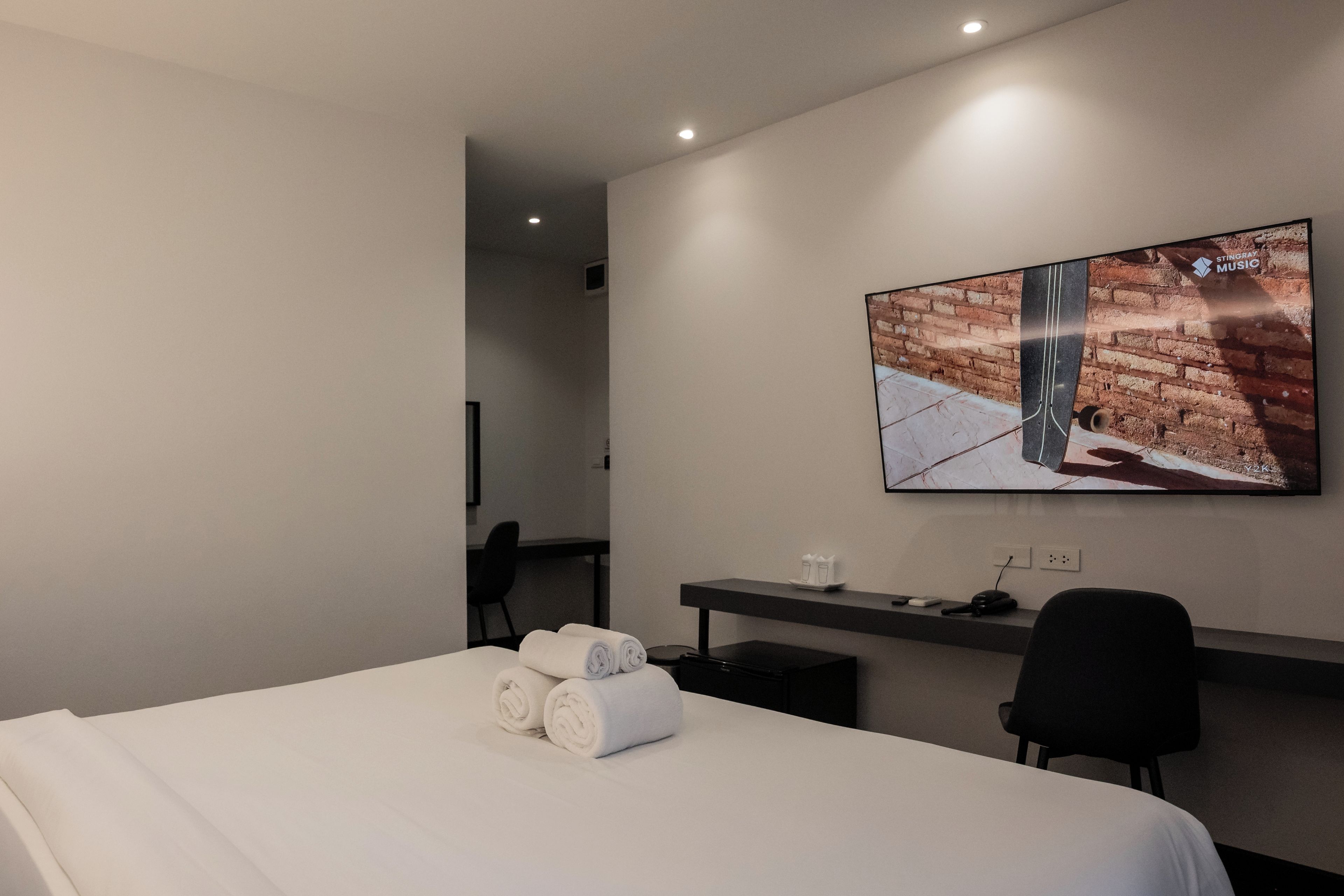 Ein Hotelzimmer mit Bett, Schreibtisch, einem an der Wand montierten Flachbildfernseher und einem kleinen Tisch mit einem Glas Wasser.
