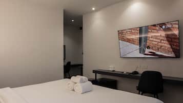 Habitación de hotel con cama, escritorio, televisor de pantalla plana montado en la pared y una mesita con un vaso de agua.
