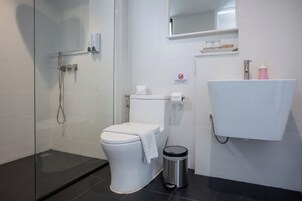 Un baño moderno con cabina de ducha de vidrio, inodoro, lavabo con dispensador de jabón y cubo de basura.