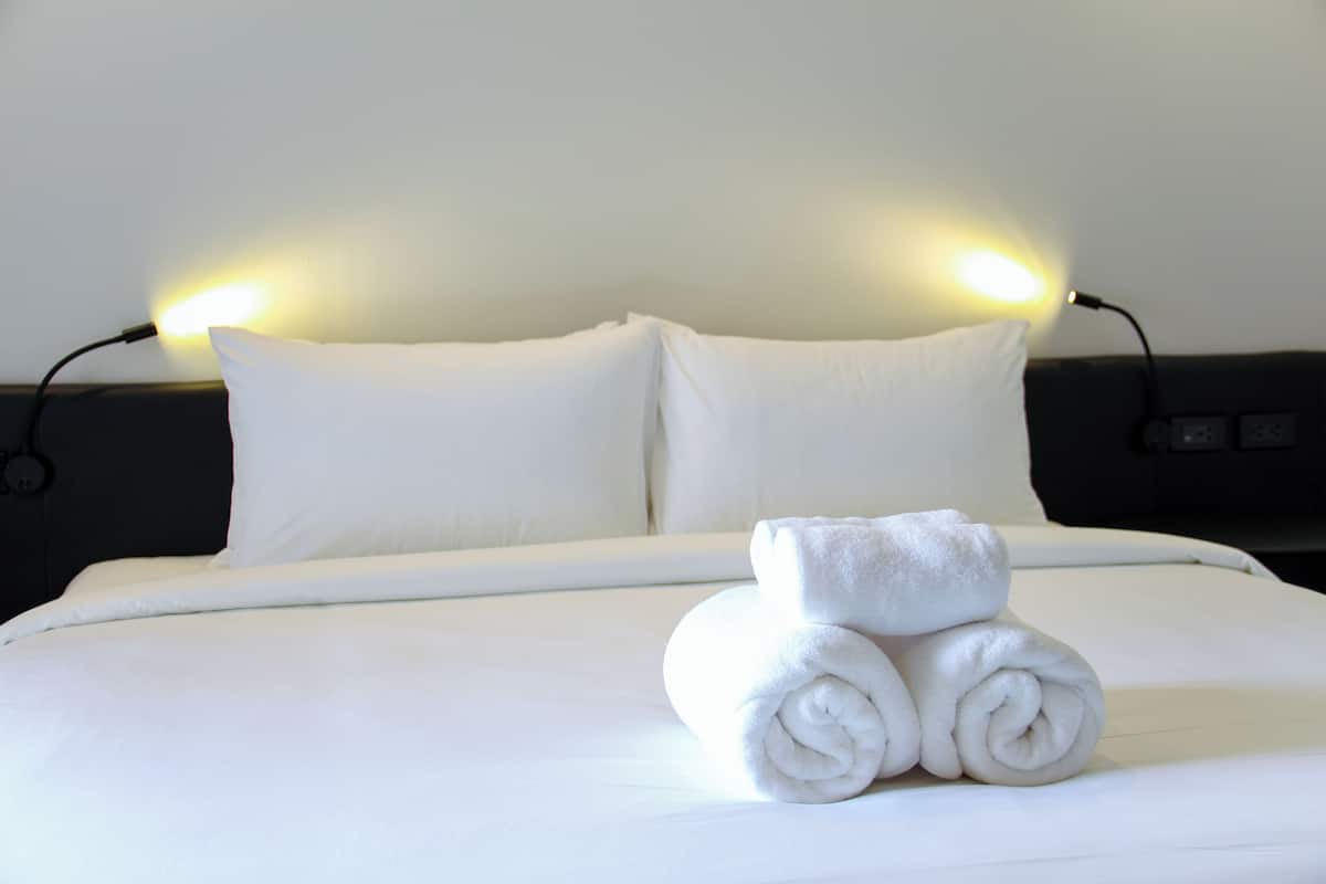 A neatly made bed with white linens and two rolled towels on top, flanked by two bedside lamps.
