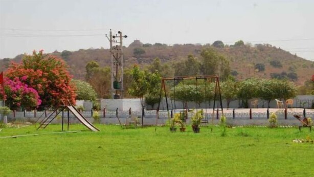 A grassy area with a playground, including a swing set and a slide. - Hotel Sambodhi (Sanchi)