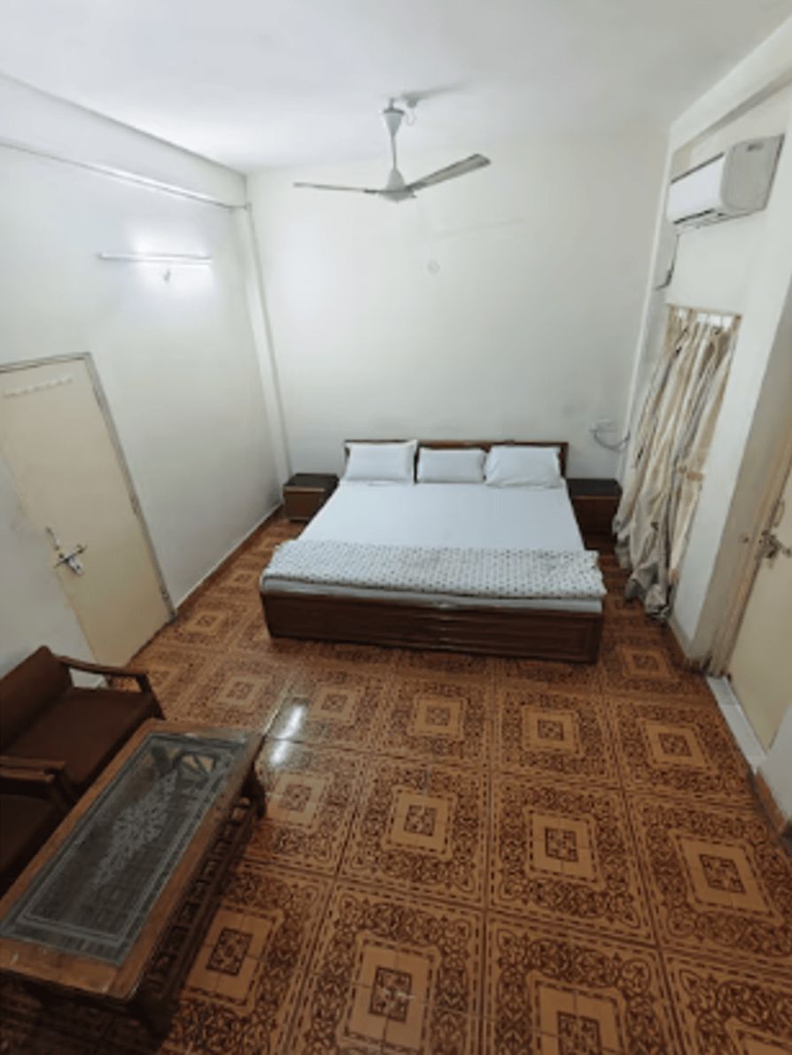 A room with a bed, a ceiling fan, a wardrobe, and a small table with a chair.