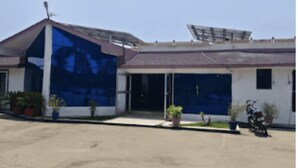 A building with a large glass facade, a covered parking area, and a motorcycle parked in front. - Hotel Sambodhi (Sanchi)