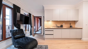 A modern apartment with a black tufted sofa, a small side table, a kitchen with white cabinets and a wooden countertop, and a sliding glass door leading to a balcony. - Apartamenty Sun & Snow Granaria (Gdansk)