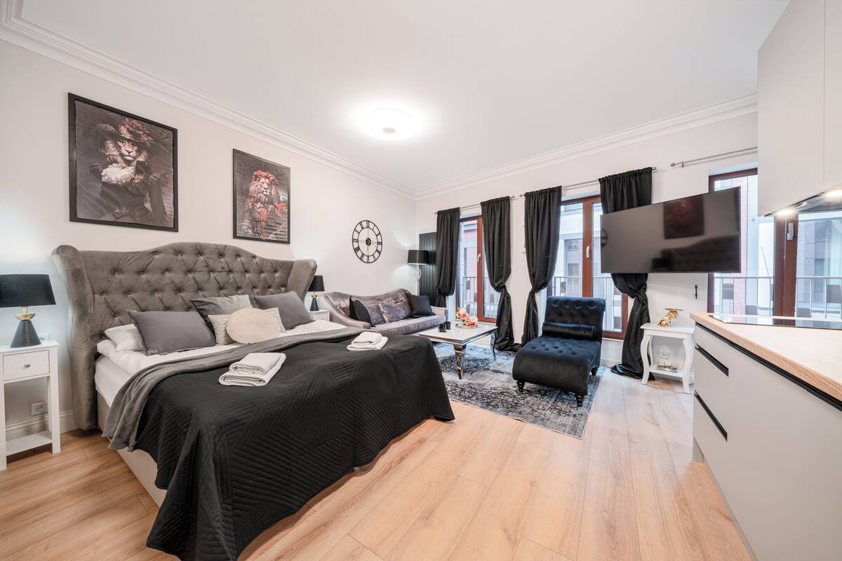 A modern bedroom with a large bed, a sofa, a TV, and a dining area.
