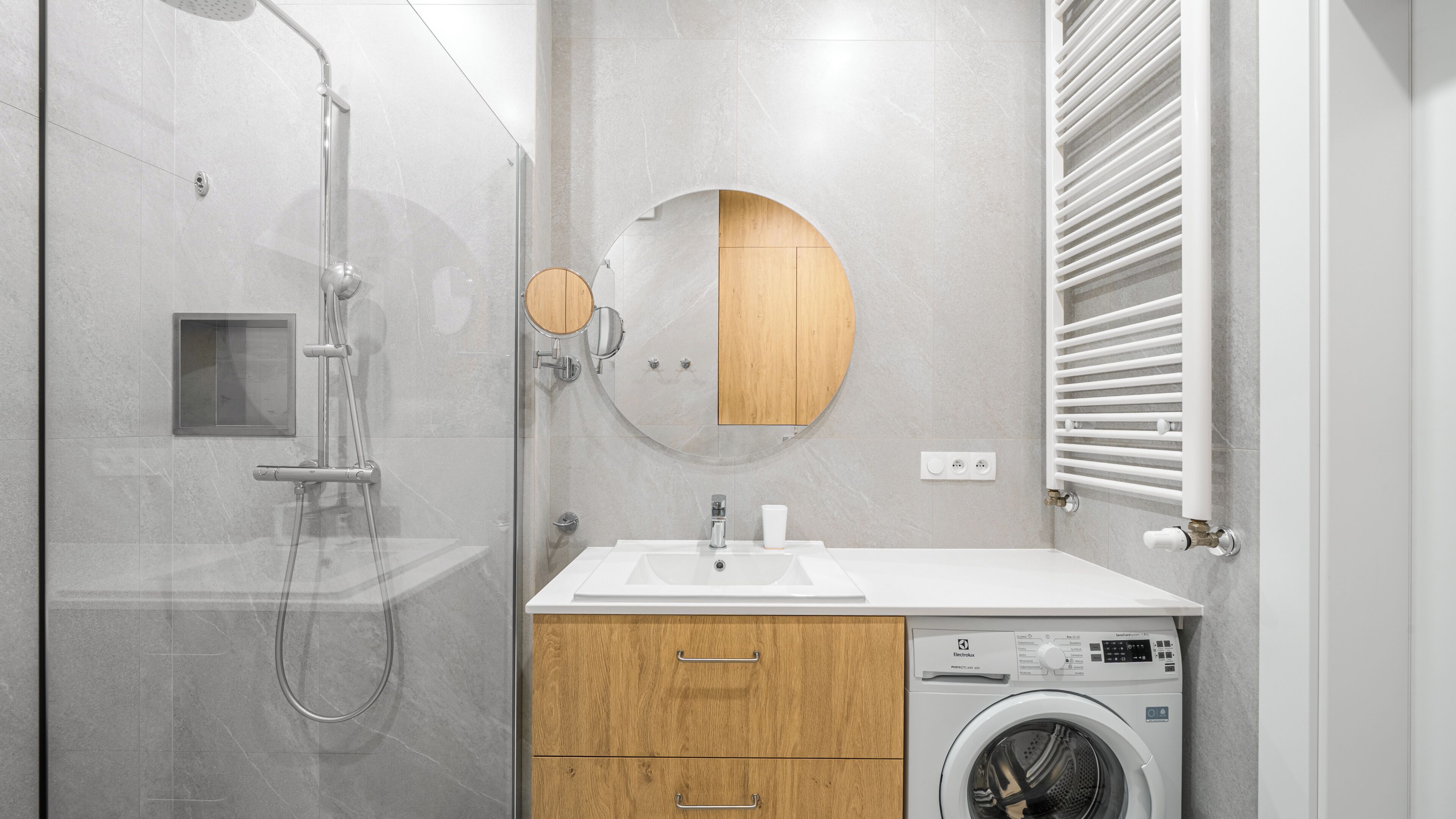 Un baño moderno con cabina de ducha de vidrio, tocador de madera con lavamanos y lavadora de carga frontal.