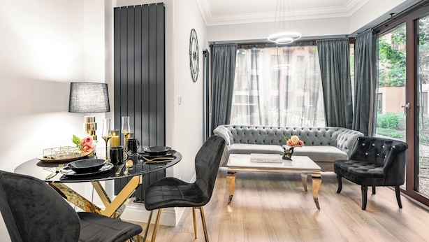 A modern living room with a grey sofa, black chairs, a coffee table, and a dining table with a lamp. - Apartamenty Sun & Snow Granaria (Gdansk)