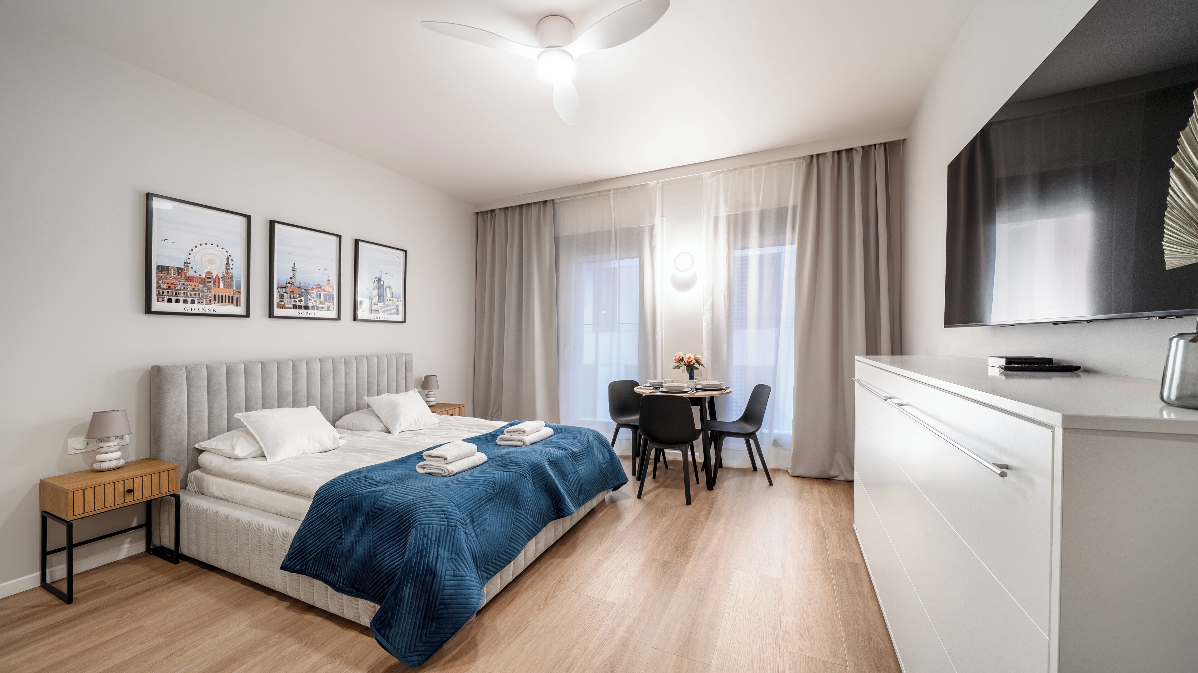 Habitación de hotel moderna con cama, mesita de noche, escritorio, sillas y televisor.