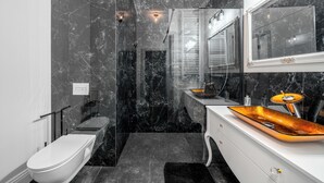 A modern bathroom with a white toilet, a glass-enclosed shower, and a vanity with a large mirror and a unique orange sink. - Apartamenty Sun & Snow Granaria (Gdansk)