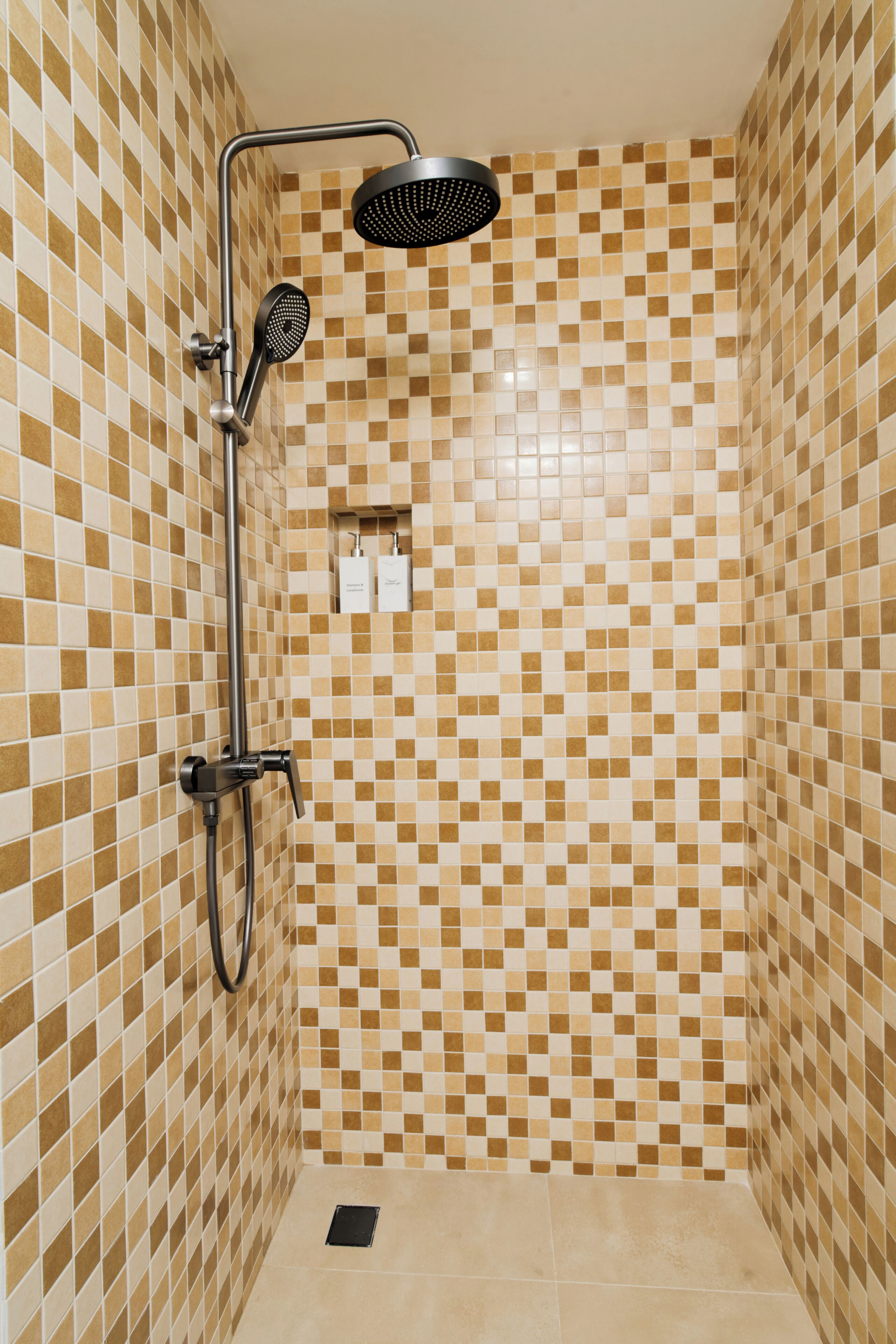 A shower with a checkered tile wall, a handheld showerhead, and a wall-mounted faucet.