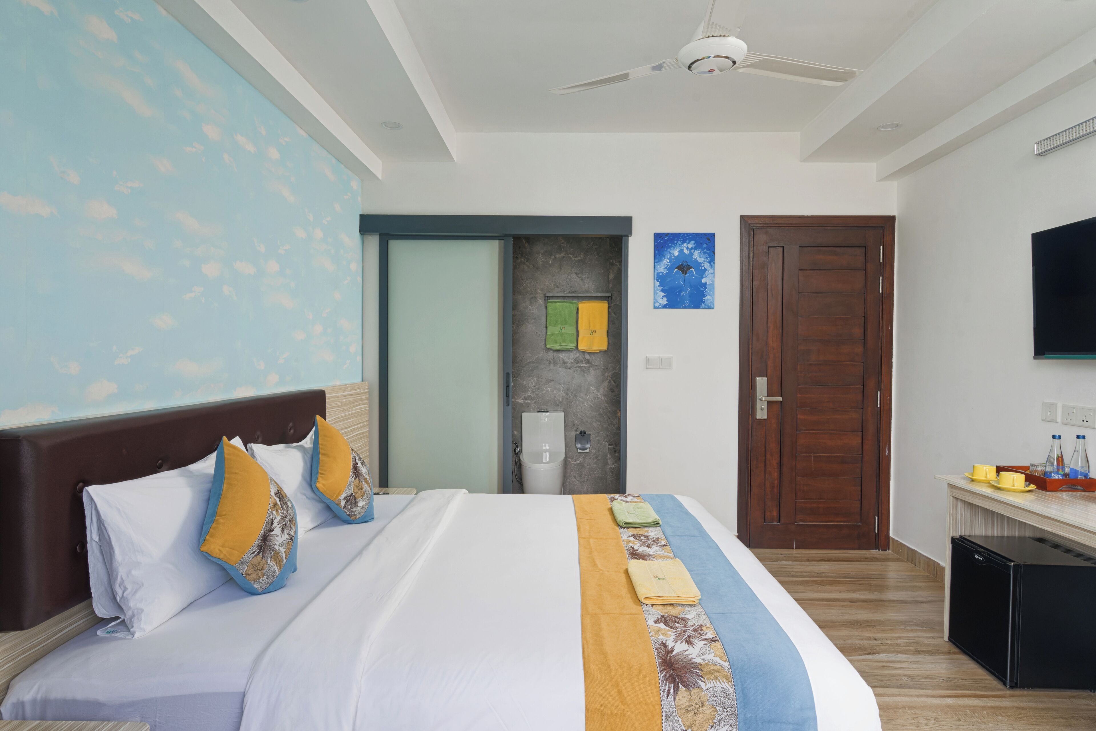 Une chambre d’hôtel avec un grand lit, un ventilateur de plafond, une télévision et une petite kitchenette.