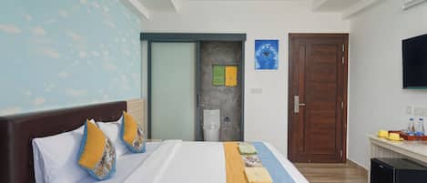 Una habitación de hotel con una cama grande, ventilador de techo, televisor y una kitchenette pequeña.