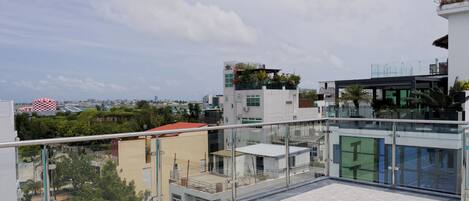 A modern building with a glass facade, a rooftop terrace, and a view of the cityscape.
