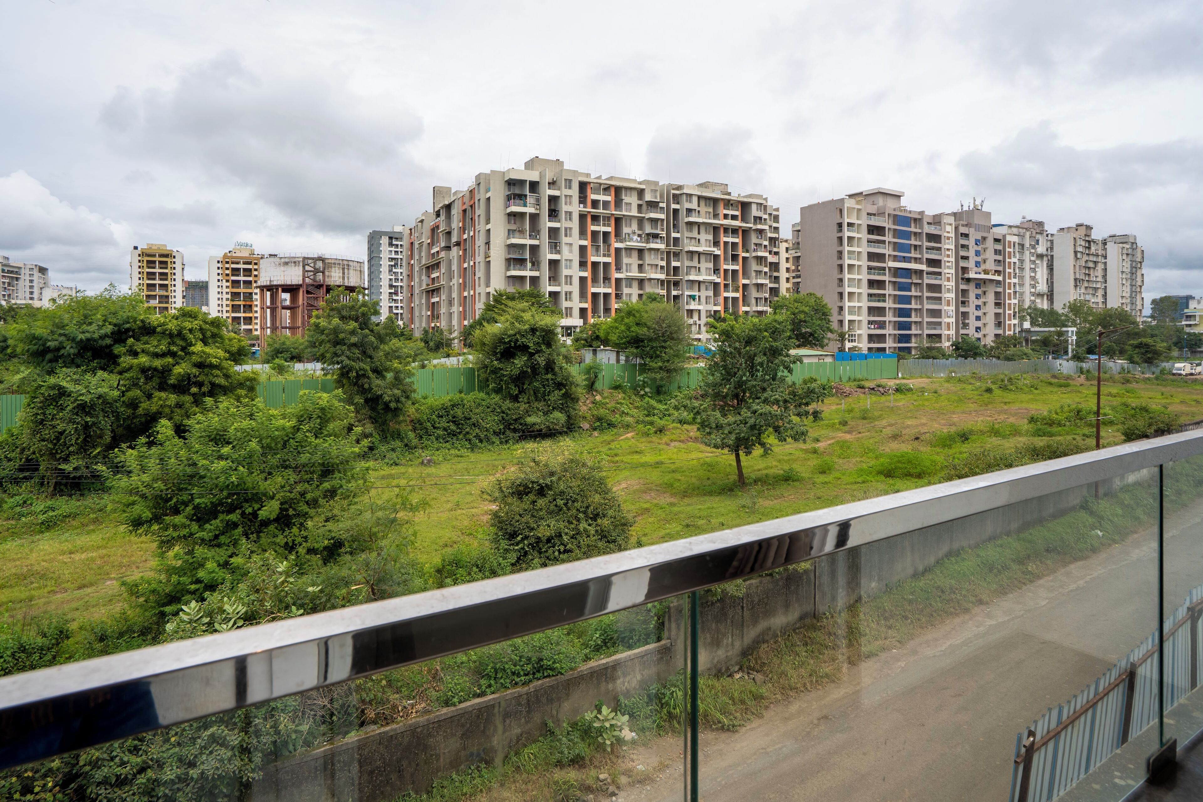 A residential building complex with multiple high-rise apartments, surrounded by greenery and a road with a concrete barrier.