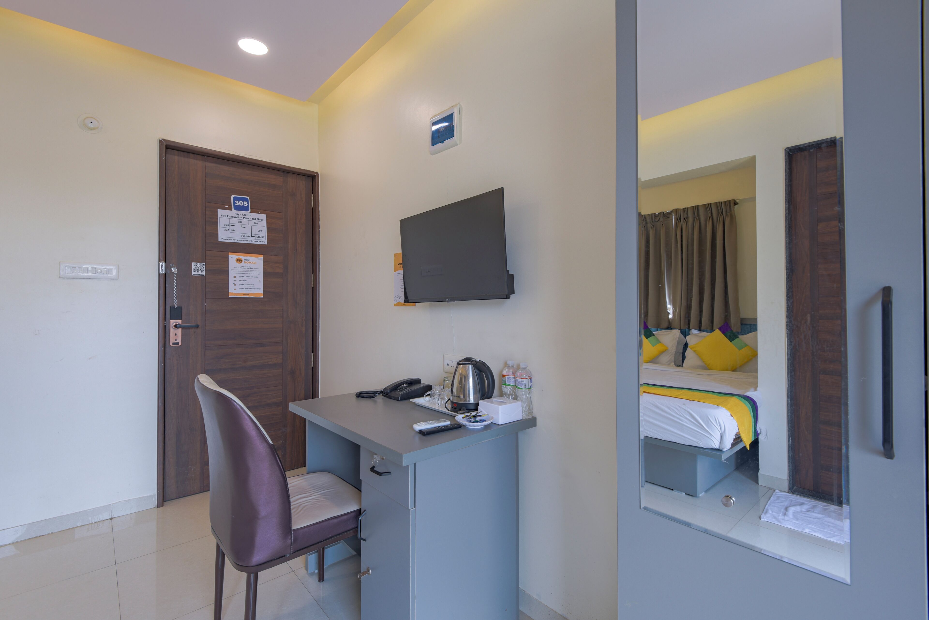 Habitación de hotel con escritorio, silla, cama, televisor y espejo.