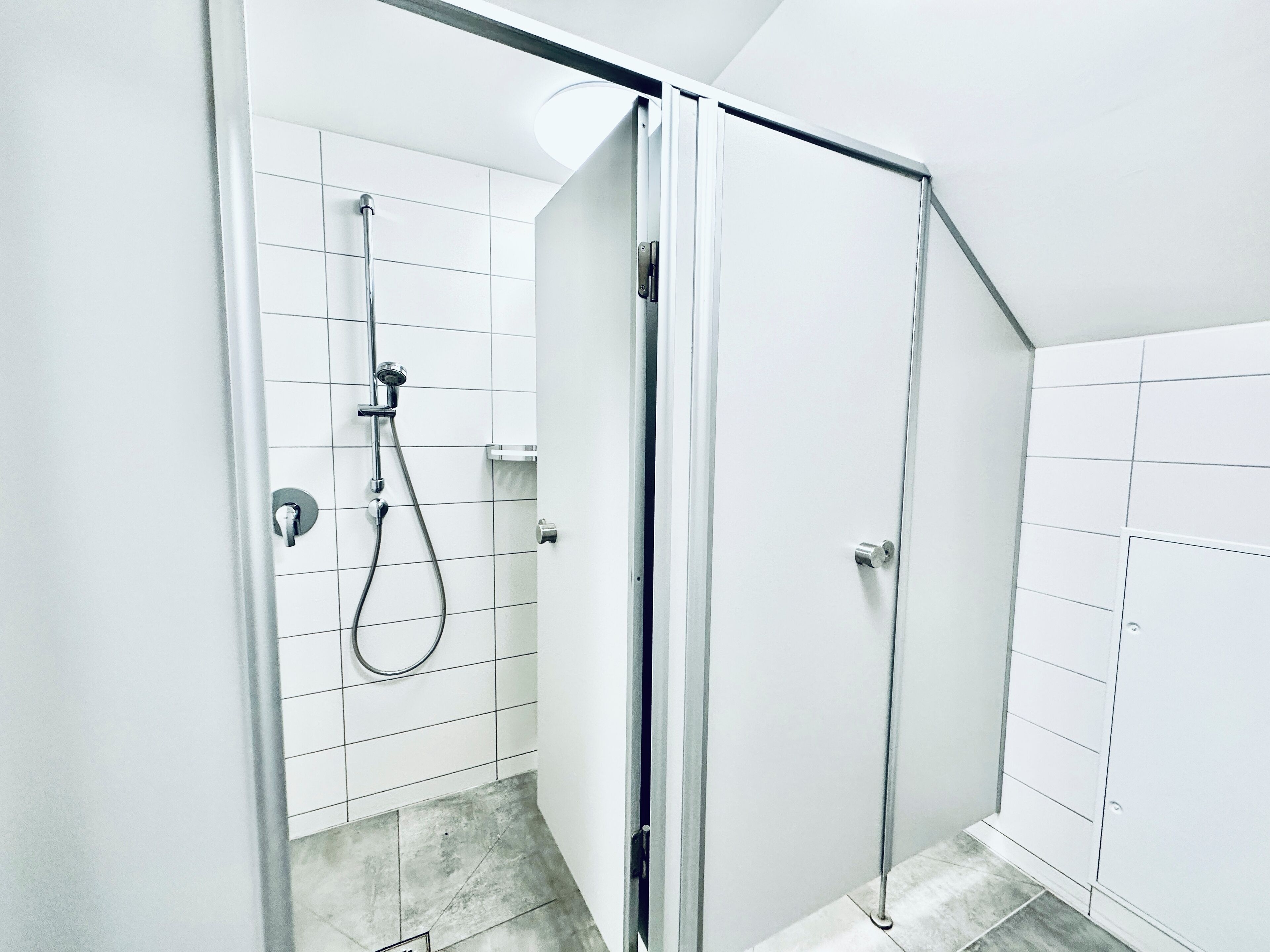 Un baño moderno con cabina de ducha de vidrio, paredes de azulejos blancos y ducha visible.