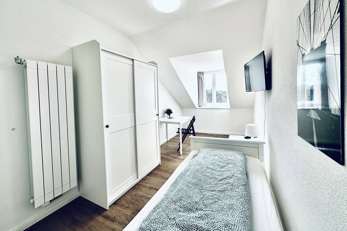 Habitació moderna i ben il·luminada amb sostre inclinat, una finestra gran, escriptori i llit.