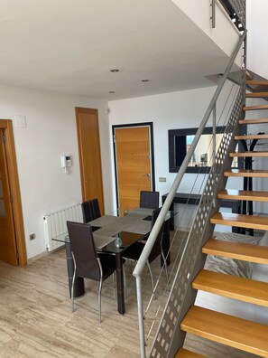 Un interno moderno con un tavolo da pranzo in vetro, sedie, una porta in legno e una scala con gradini in legno e ringhiere metalliche.