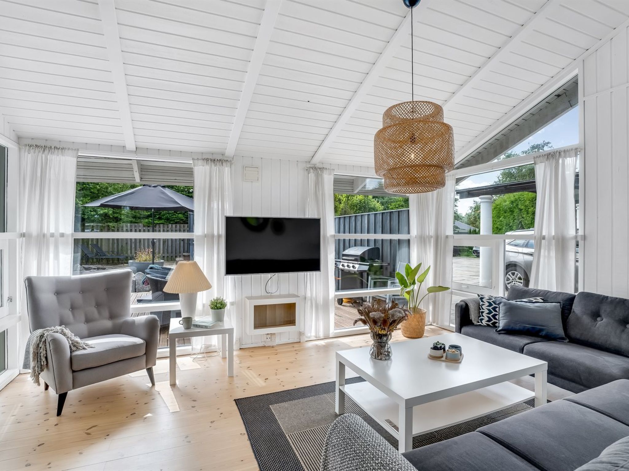 A modern living room with a TV, sofa, armchair, coffee table, and a large window overlooking a backyard.