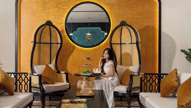 A room with a sofa, two chairs, a coffee table, and a decorative wall with a circular mirror. - Fusion Point Hotel (Hue)